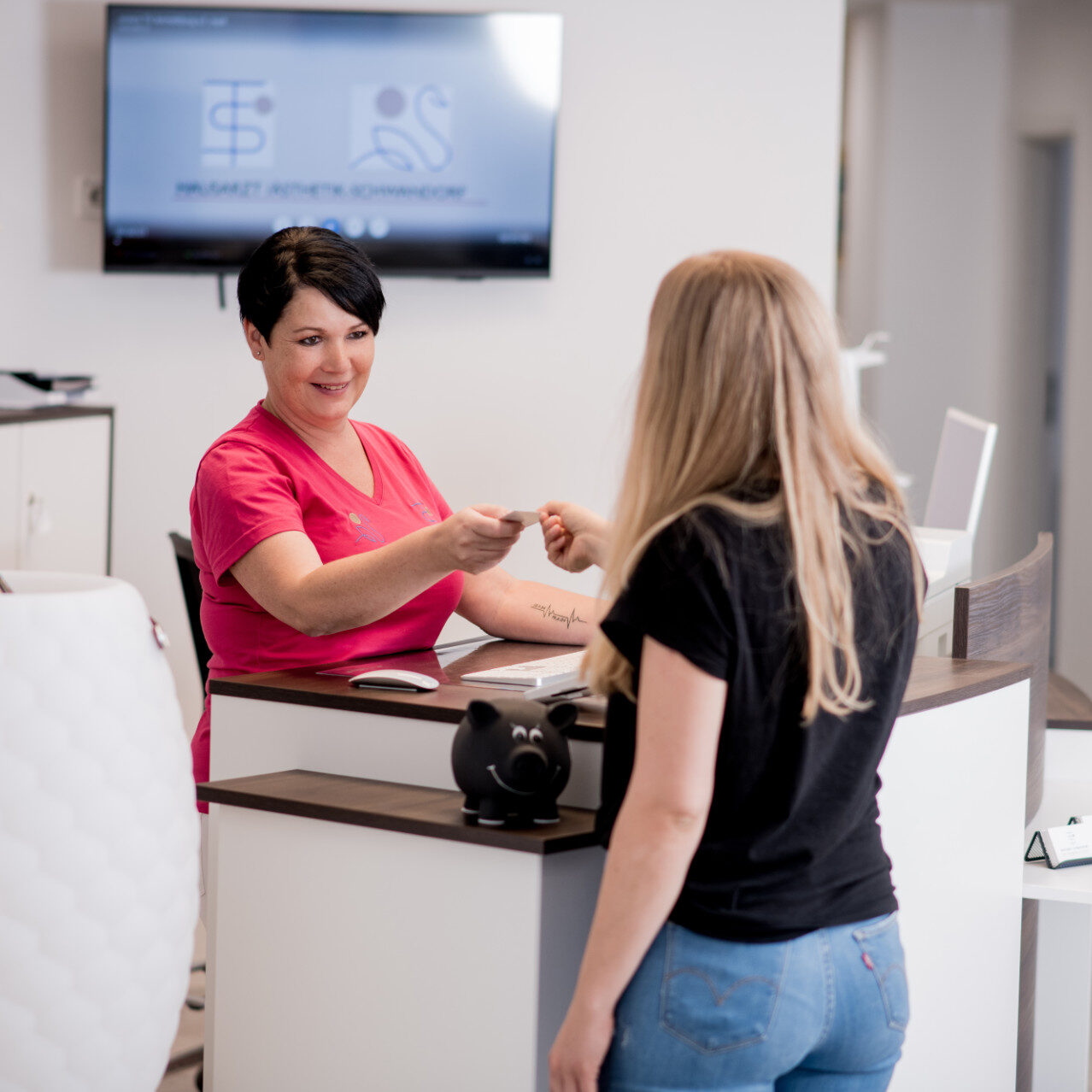 Angestellte übergibt Patientin an der Rezeption eine Visitenkarte